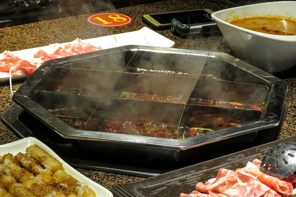 A divided Chongqing hotpot with red broth and several cooking compartments.