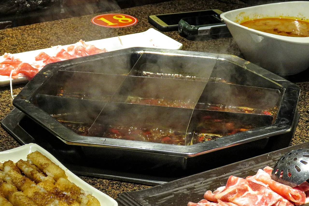 A divided Chongqing hotpot with red broth and several cooking compartments.