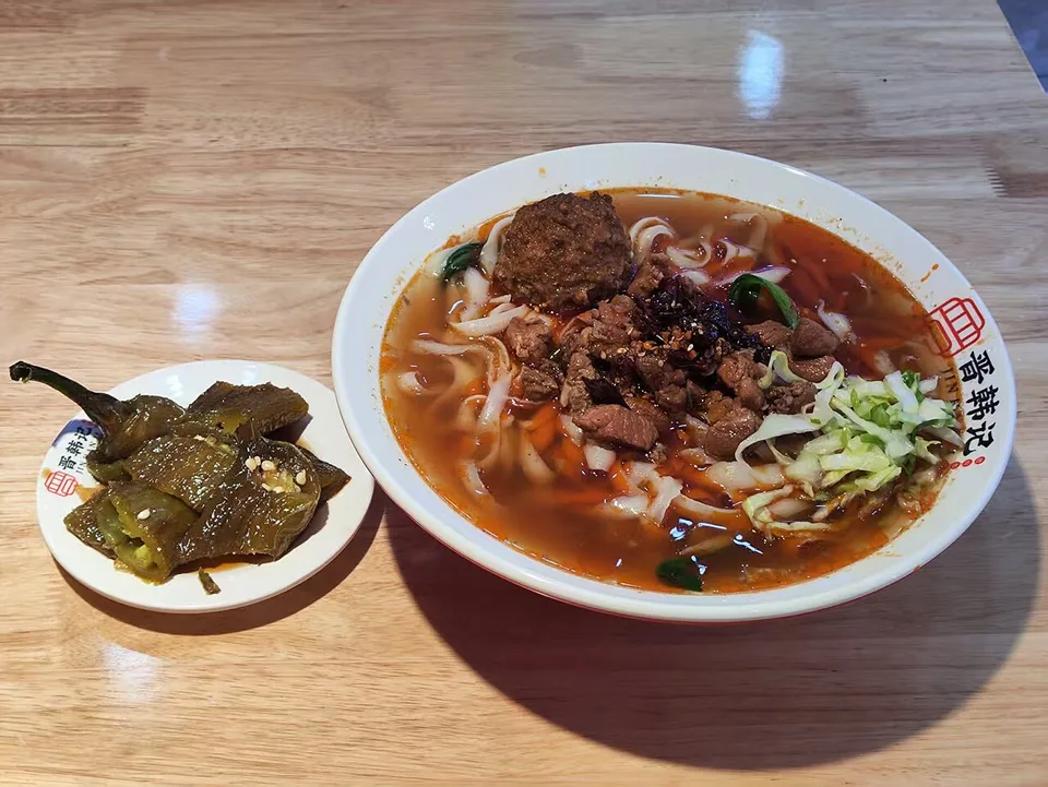 A bowl of broad knife-shaved noodles with broth and toppings.