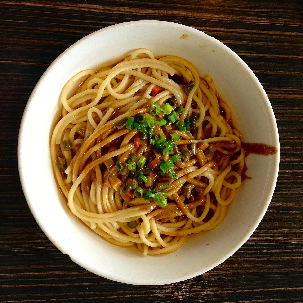 A bowl of hot-dry noodles topped with chopped green onion.