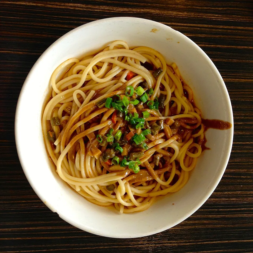 A bowl of hot-dry noodles topped with chopped green onion.