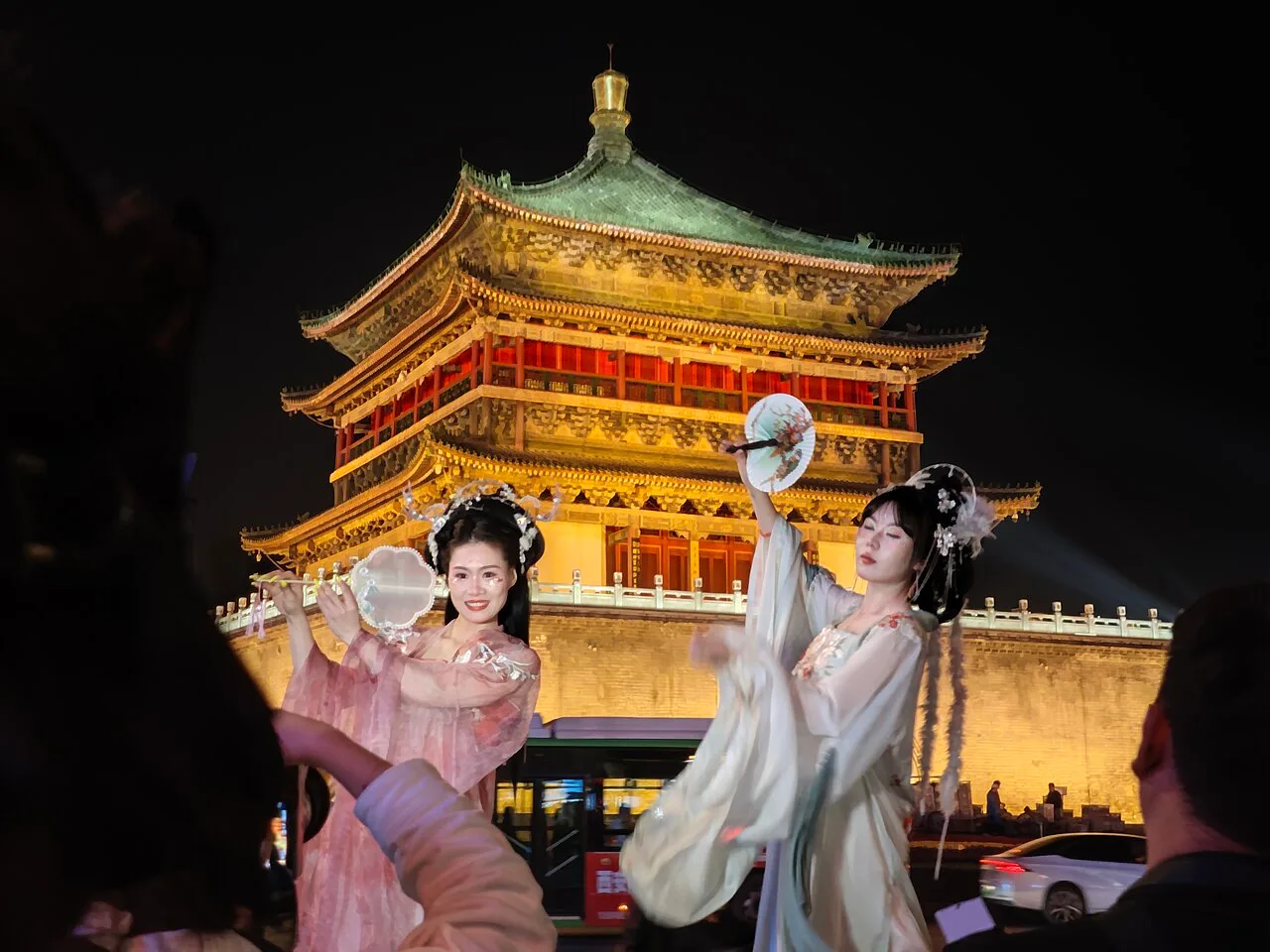 Two visitors in Hanfu posing for photographs near Xi’an’s illuminated Bell Tower.
